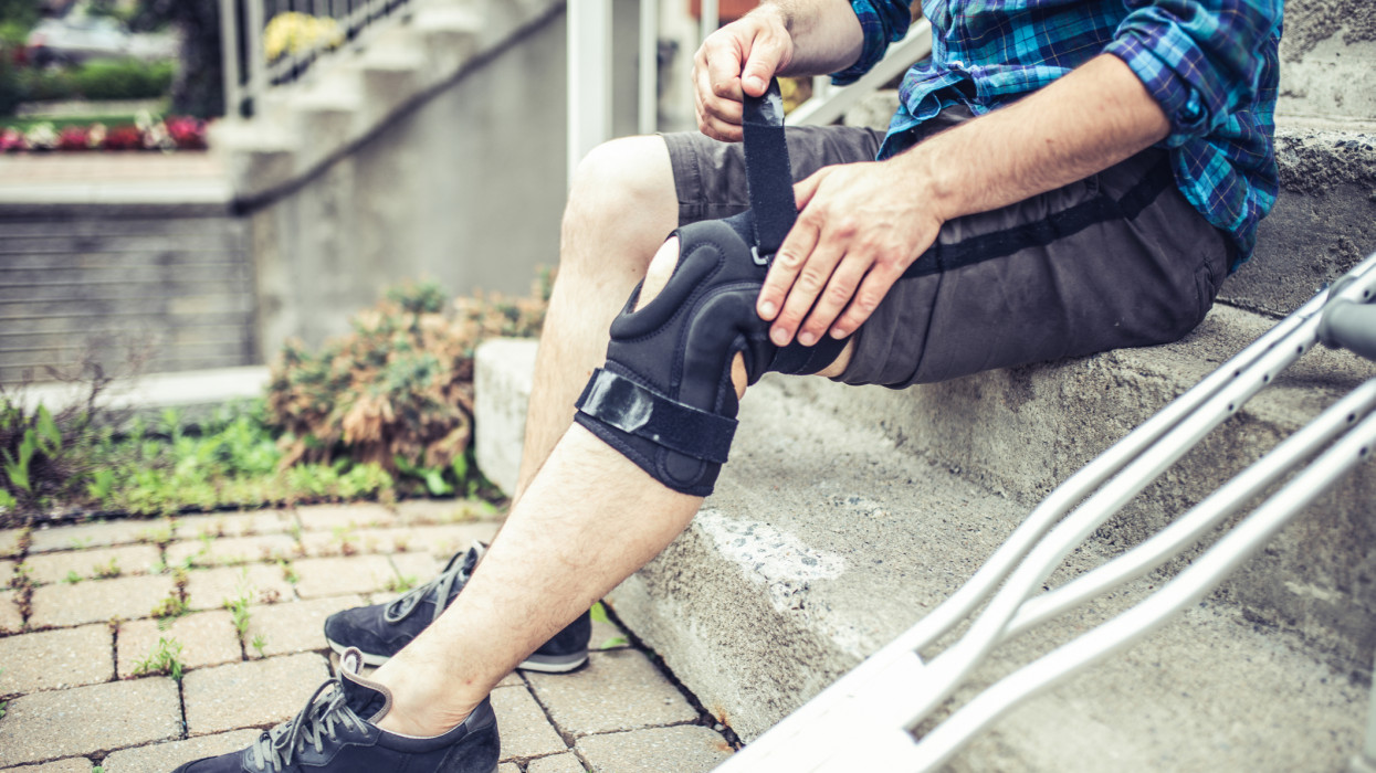man sitting on the steps and adjusting his orthosis after having knee sprain accident while playing soccer