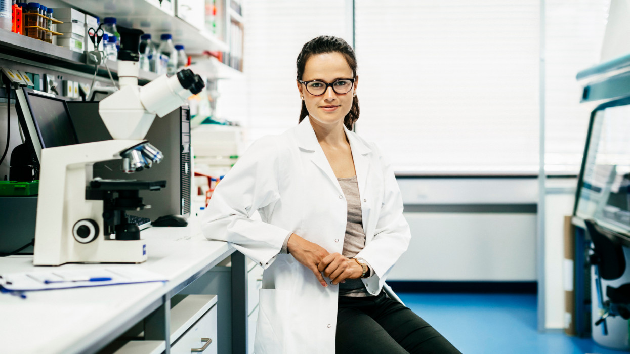 A portrait of a scientist leaning on a desk in her laboratory.