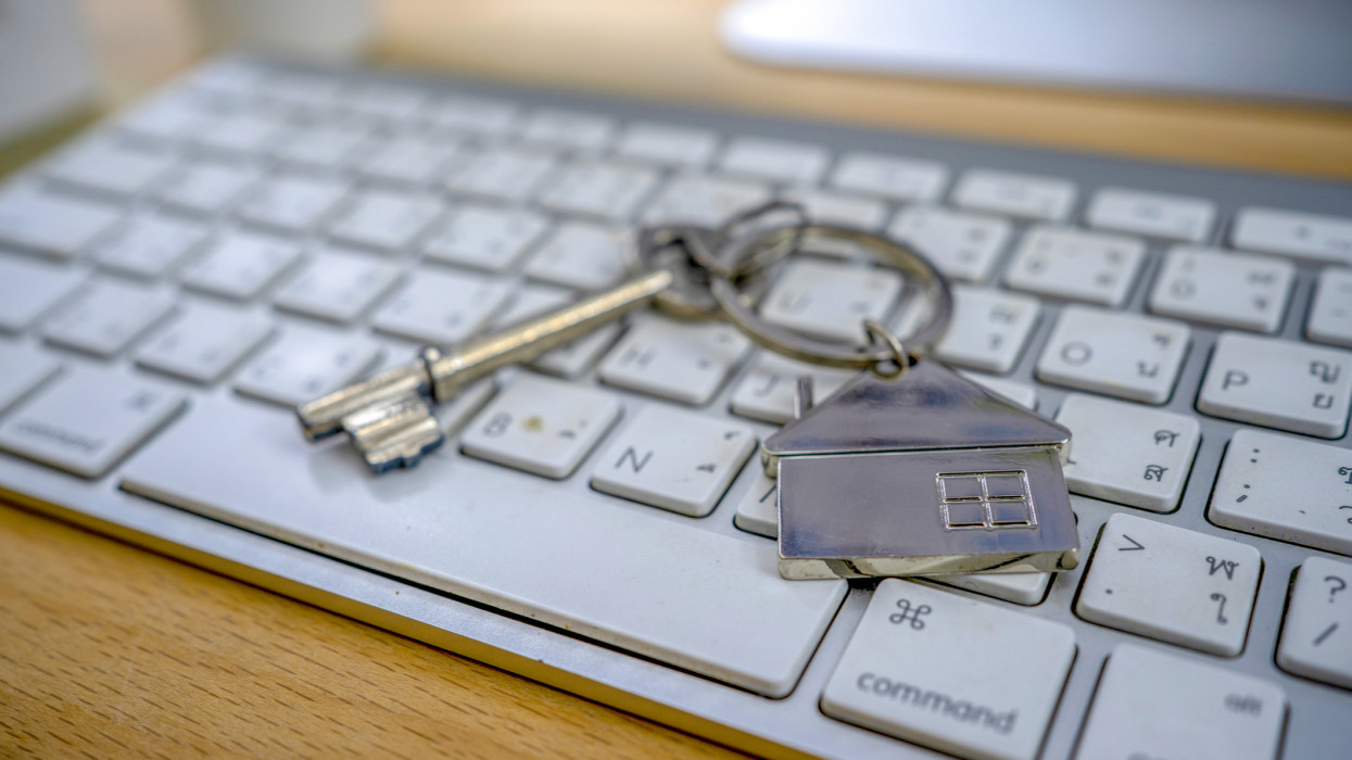 Mortgage concept with key and house-shaped keyring on laptop keyboard.