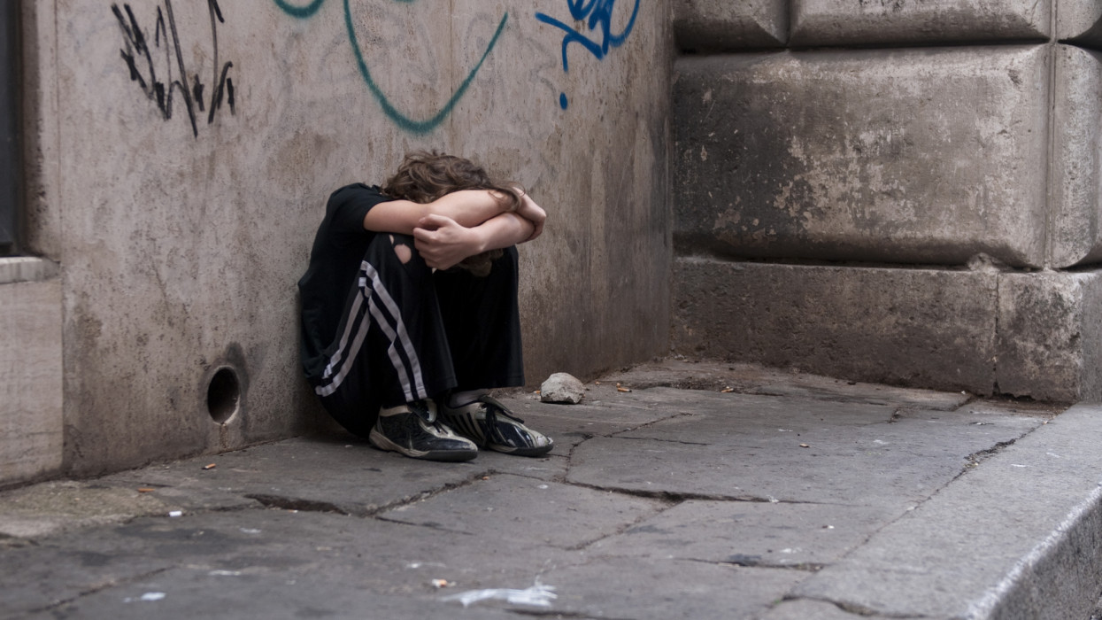 Young boy huddled and alone on a city street in Rome. Related: