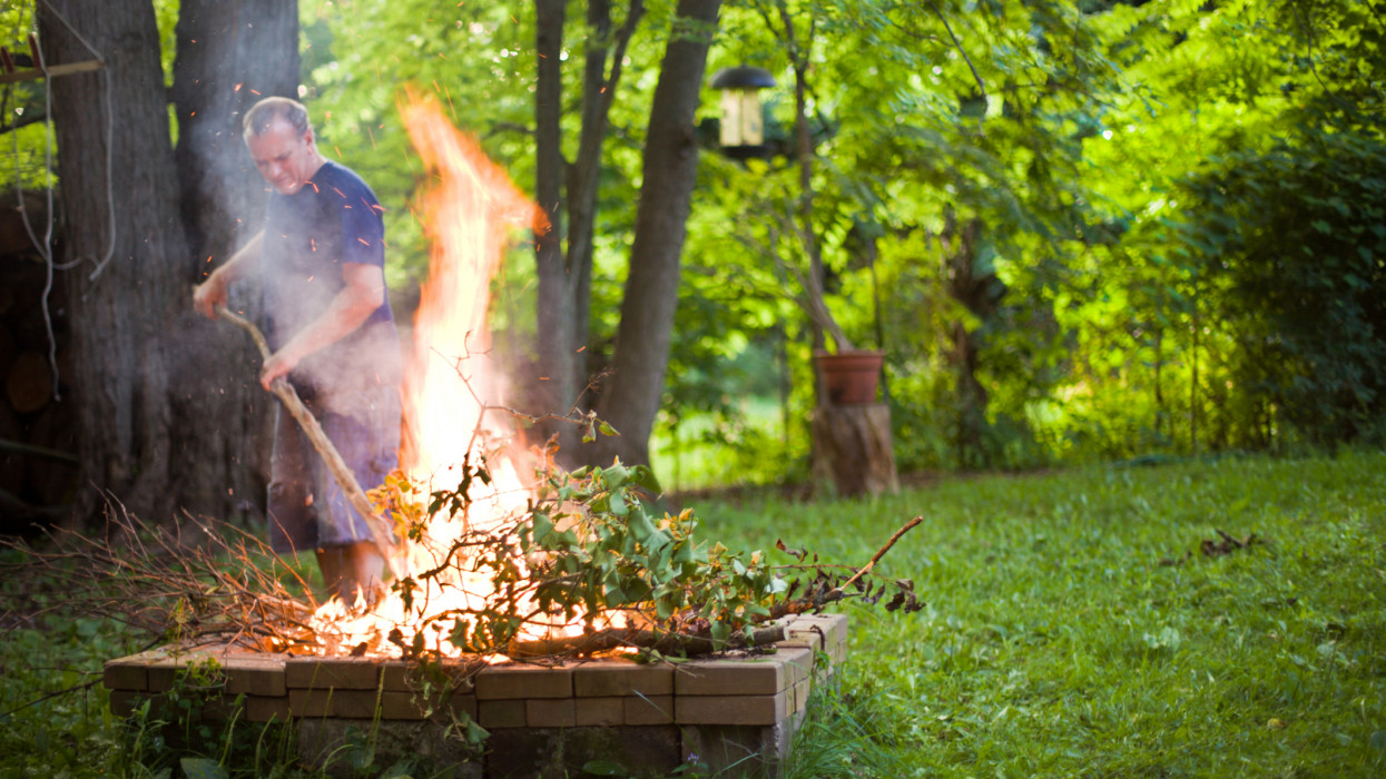 Man stoking a  bonfire with a stick in a yard.