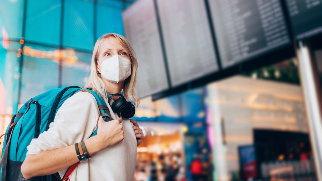 Portrait of a young woman checks the arrivals and departures board at the airport. She wears a face mask for protection during a Coronavirus pandemic.New normal lifestyle for public transport after Covid-19
