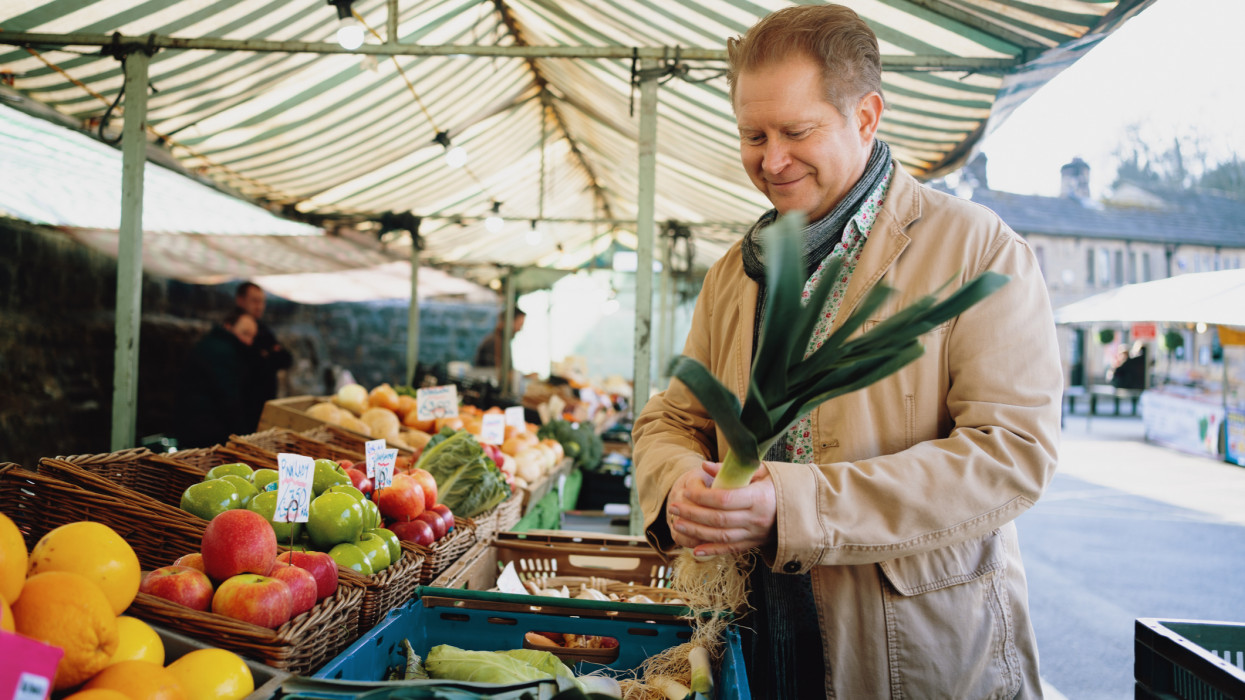 Man with short blonde hair buying a leek at vegetable stall on outdoor market