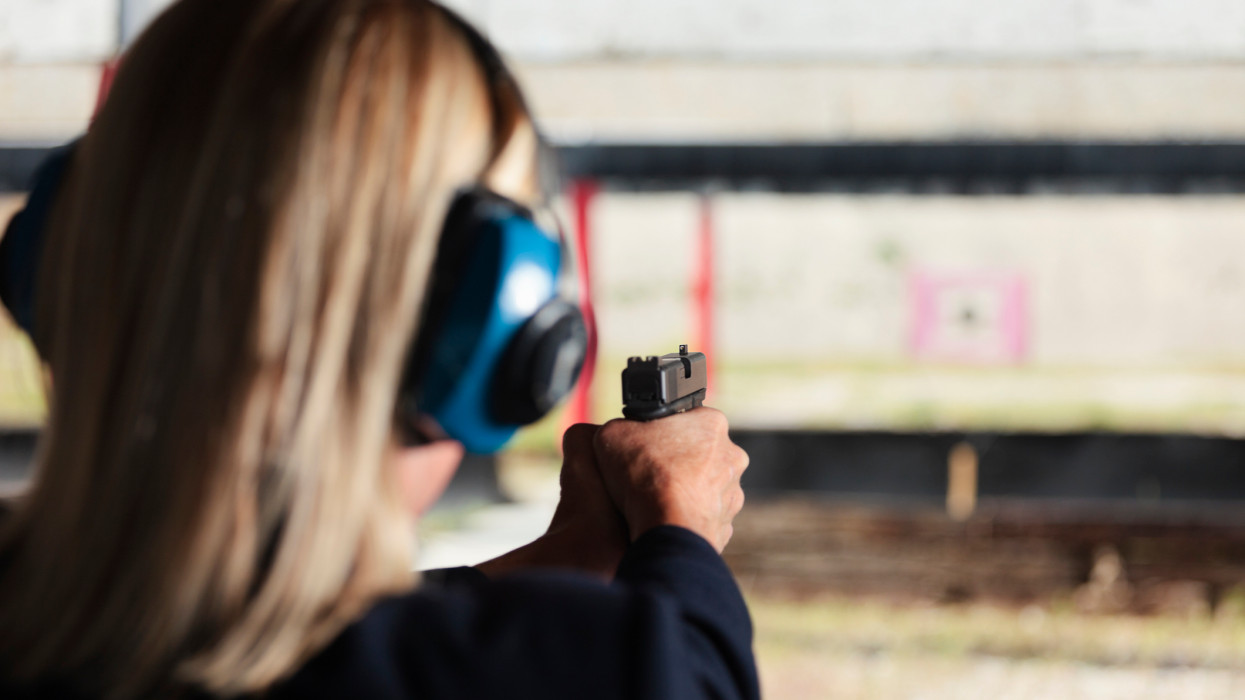 A woman at the shooting range aiming a gun at the target.
