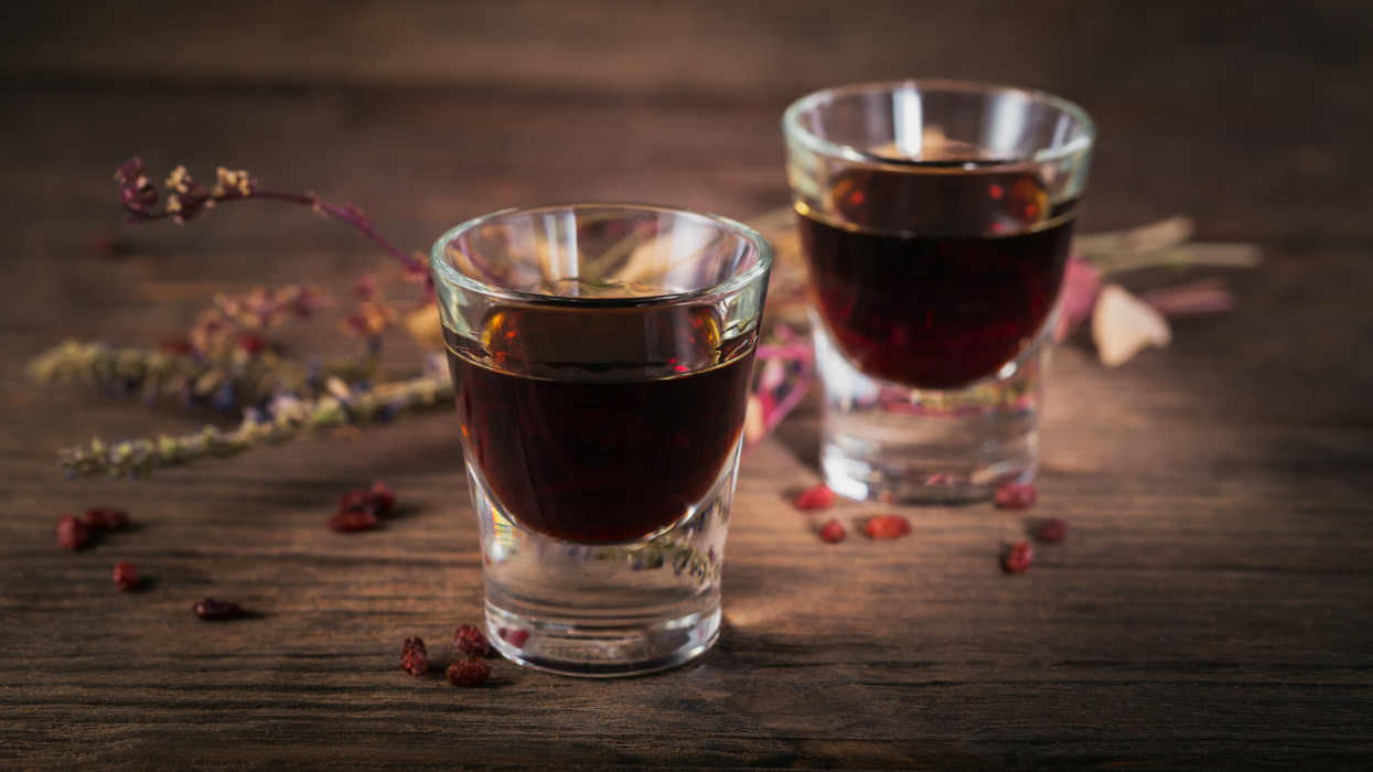Two glasses of alcoholic drink on dark wooden background. Herbal bitter liqueur with different natural ingredients.