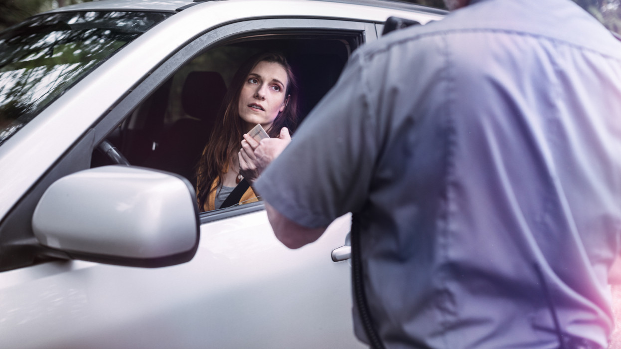 An on duty law enforcement officer, working hard at providing justice, keeping the peace, and making the country a safer place.  Here he inspects the drivers license of a person he has pulled over for speeding, given them a stern warning about the risk and danger of their behavior and the cost of a potential ticket.