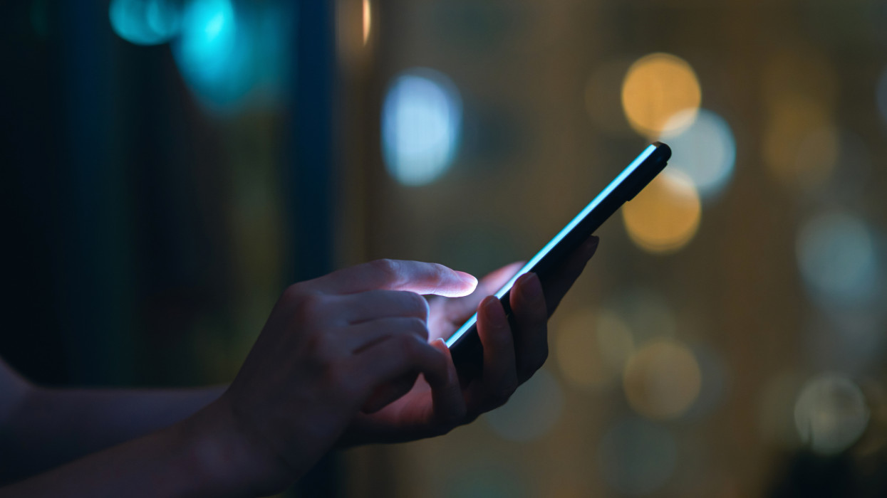 Close up of womans hand using smartphone in the dark, against illuminated city light bokeh