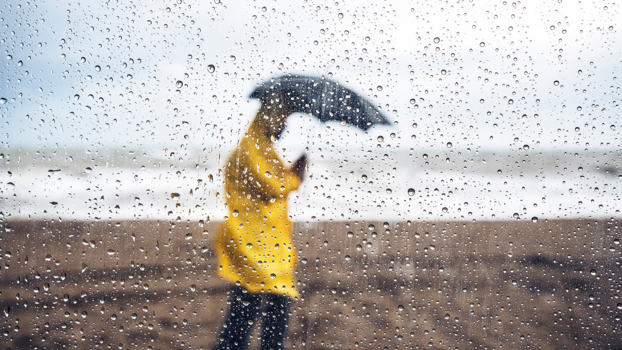 Man walking on the beach under heavy rain, viewed through windshield with raindrops