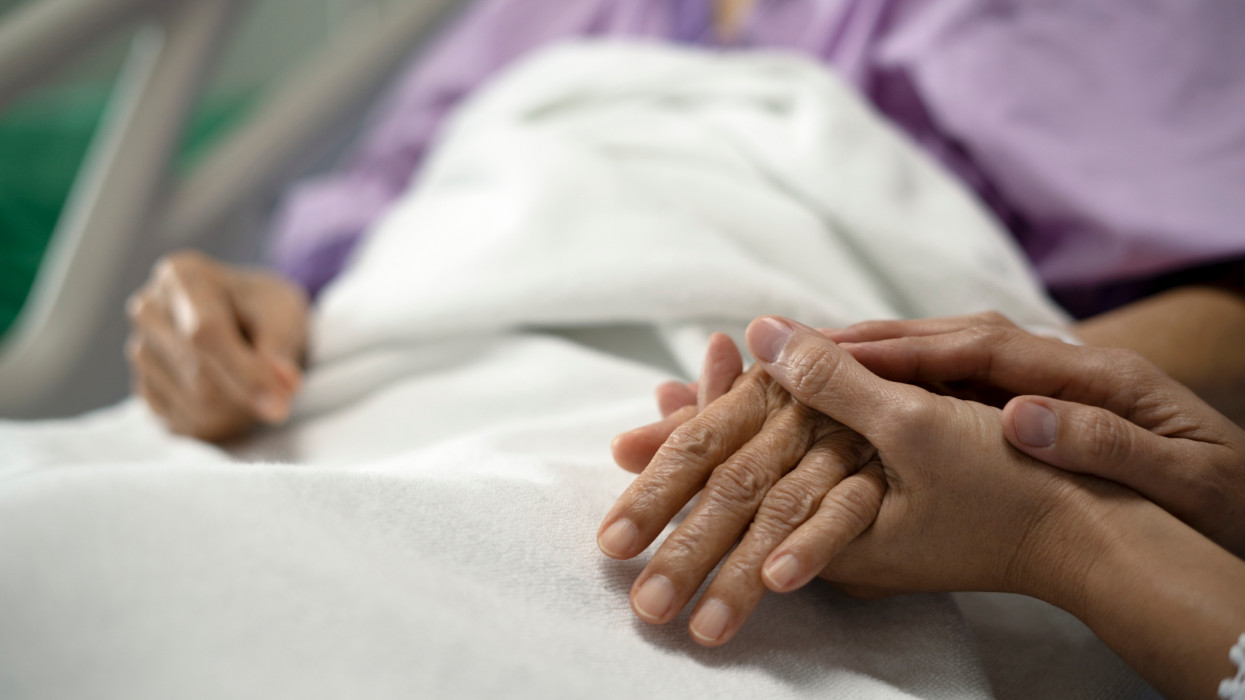 Image of daughter holding the mothers hand and encourage while her mother sitting on bed in hospital.