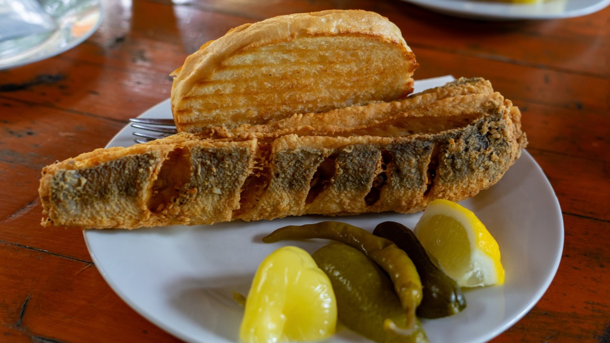 Balaton style hake ( balatoni hekk ) breaded deep fried fish at a restaurant with sour vegetables pickle and garlic bread toast a typical popular hungarian summer food .