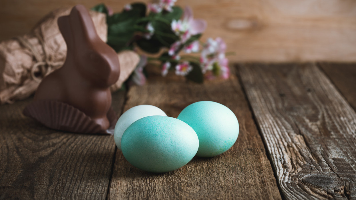 Happy Easter greeting with chocolate bunny and eggs on wooden background