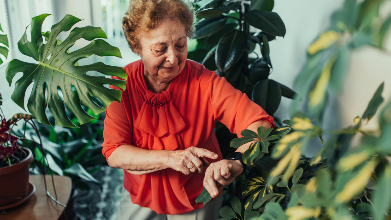 Senior woman checking her watch while standing in terrace surrounded by plants at home