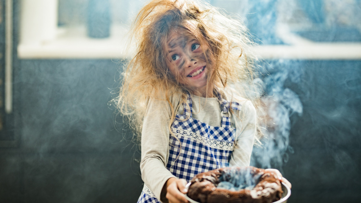 Happy little girl with messy hair holding burnt the cake in the kitchen.