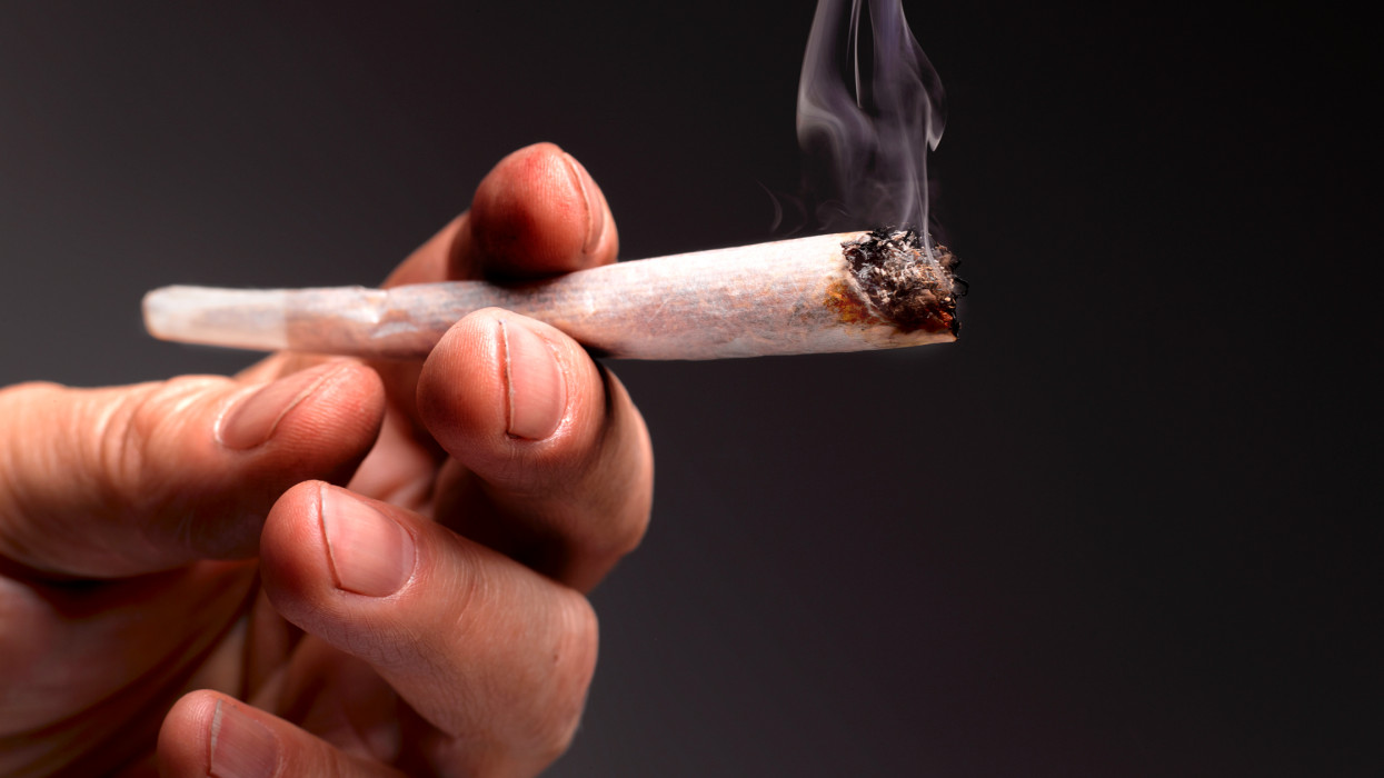 dirty fingernails and hands of drug addict holding lit marijuana joint