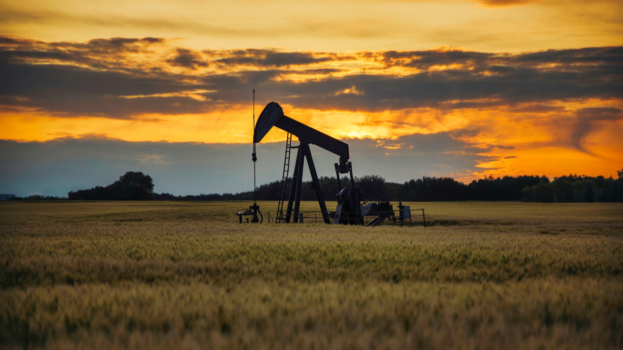 An oil pump jack on the middle of the wheat field with the beautiful sunset sky. A pump jack is a device used in the petroleum industry to extract crude oil from an oil well where there is not high enough pressure in the well to force the oil to the surface.