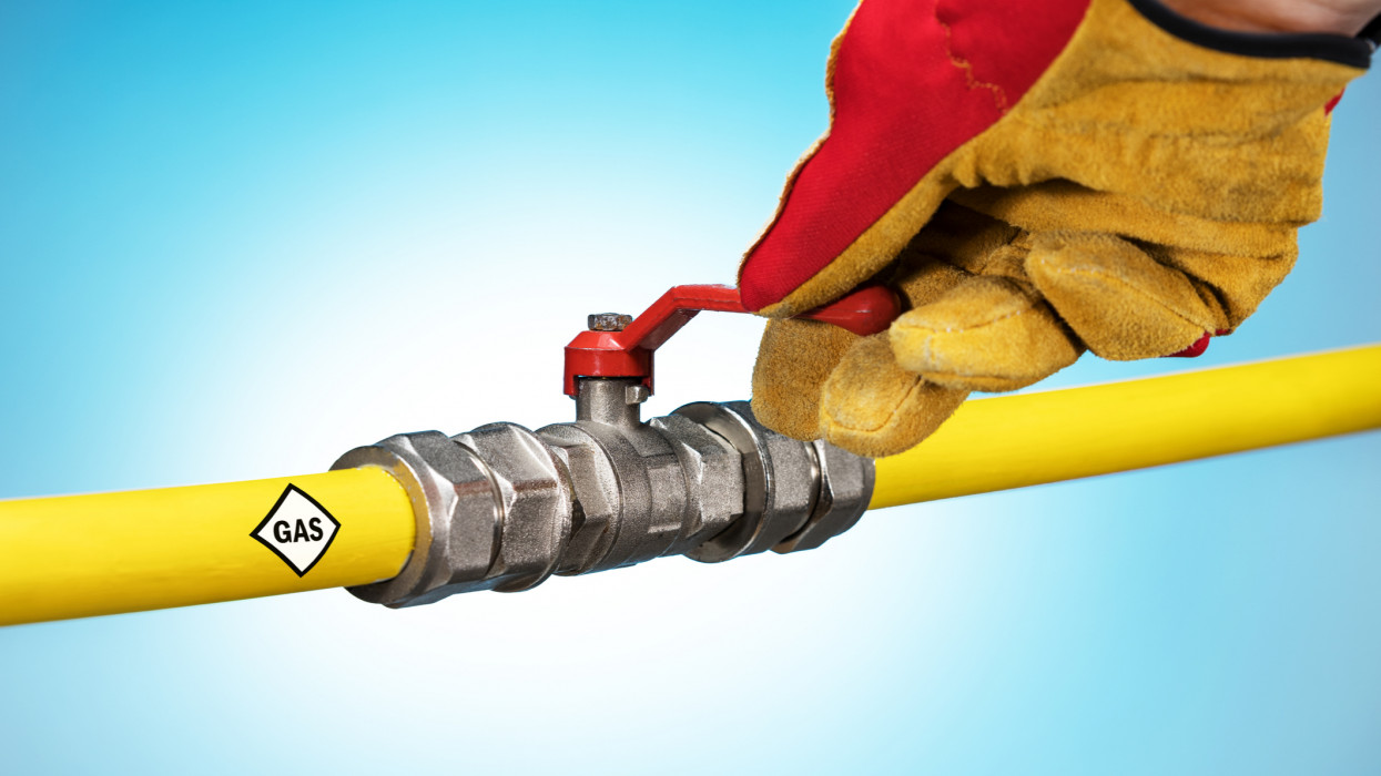 Hand Adjusting Gas Valve. Saving Gas Concept. Male hand in glove closed fauset on yellow pipe.