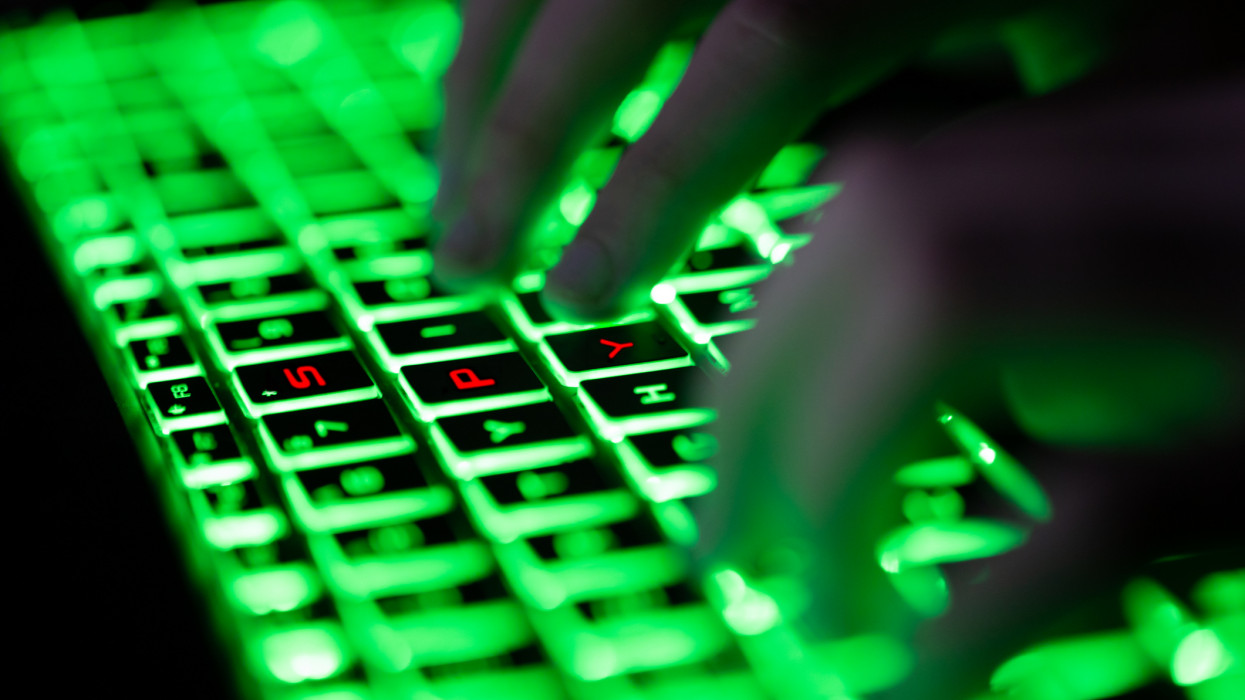 Digital composite of glowing green keyboard in the dark, the hands of a computer hacker typing and letters SPY in red on the keyboard