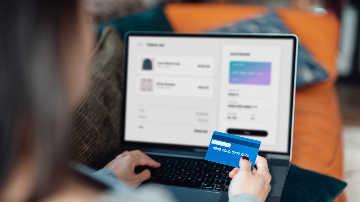 Above the shoulder view of a woman shopping clothes online on laptop, making payment with credit card. Enjoying seasonal sales. Shopaholic concept. Cyber security idea. Close up shot. Laptop screen mockup.