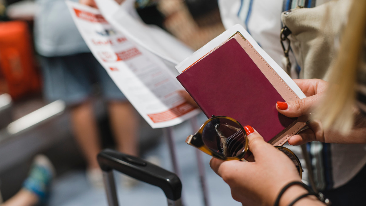 Close up shot of a mid adult woman holding her travel documents, passport and sunglasses in the airport.