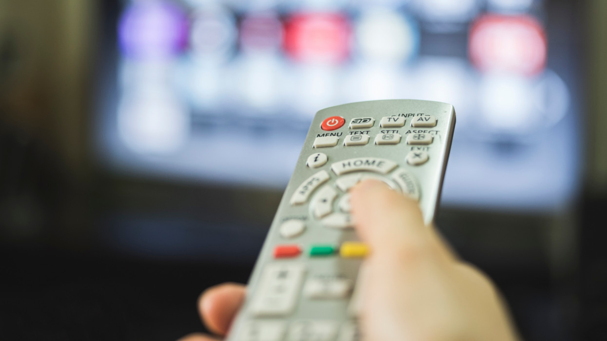 A hand changing television channels with the remote control