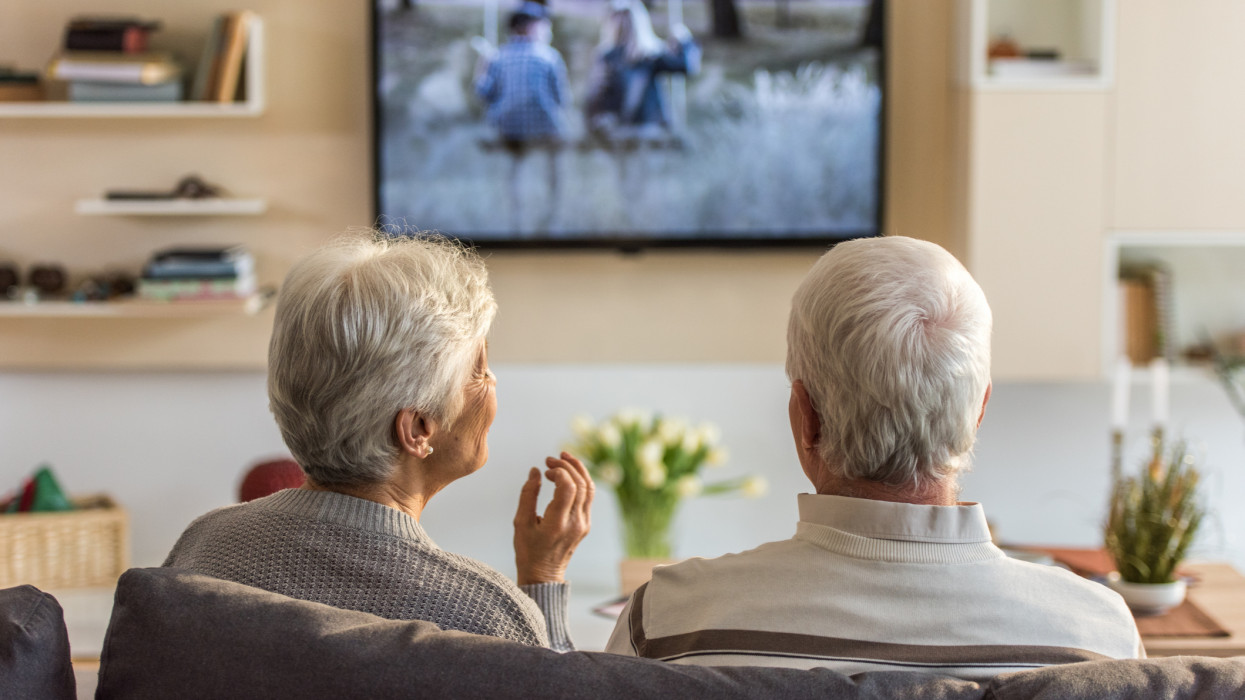 Senior couple sitting on sofa and watching television show at home.