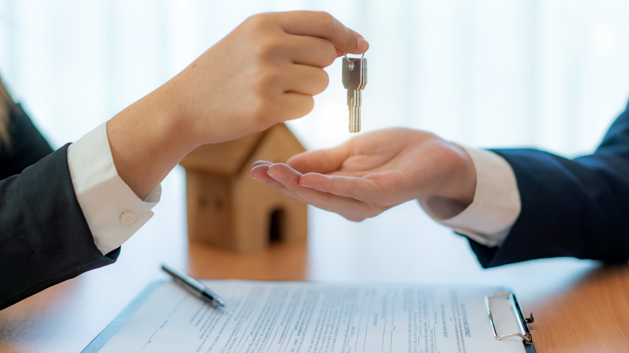 Woman real estate agent handing over keys of new house giving house keys to man after signing rental lease contract of sale purchase agreement, concerning mortgage loan offer for and house insurance.
