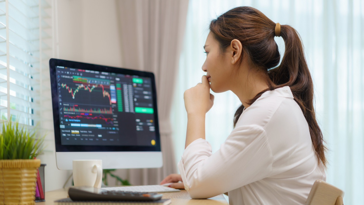 Asian woman are sitting at their desks at home trading stocks or cryptocurrency. In the living room at home. People handling various aspects of their finances from home. Depicts TradingView financial market chart.