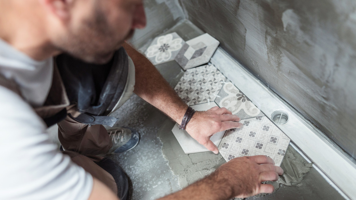 High angle image of male builder installing tiles on the bathroom floor
