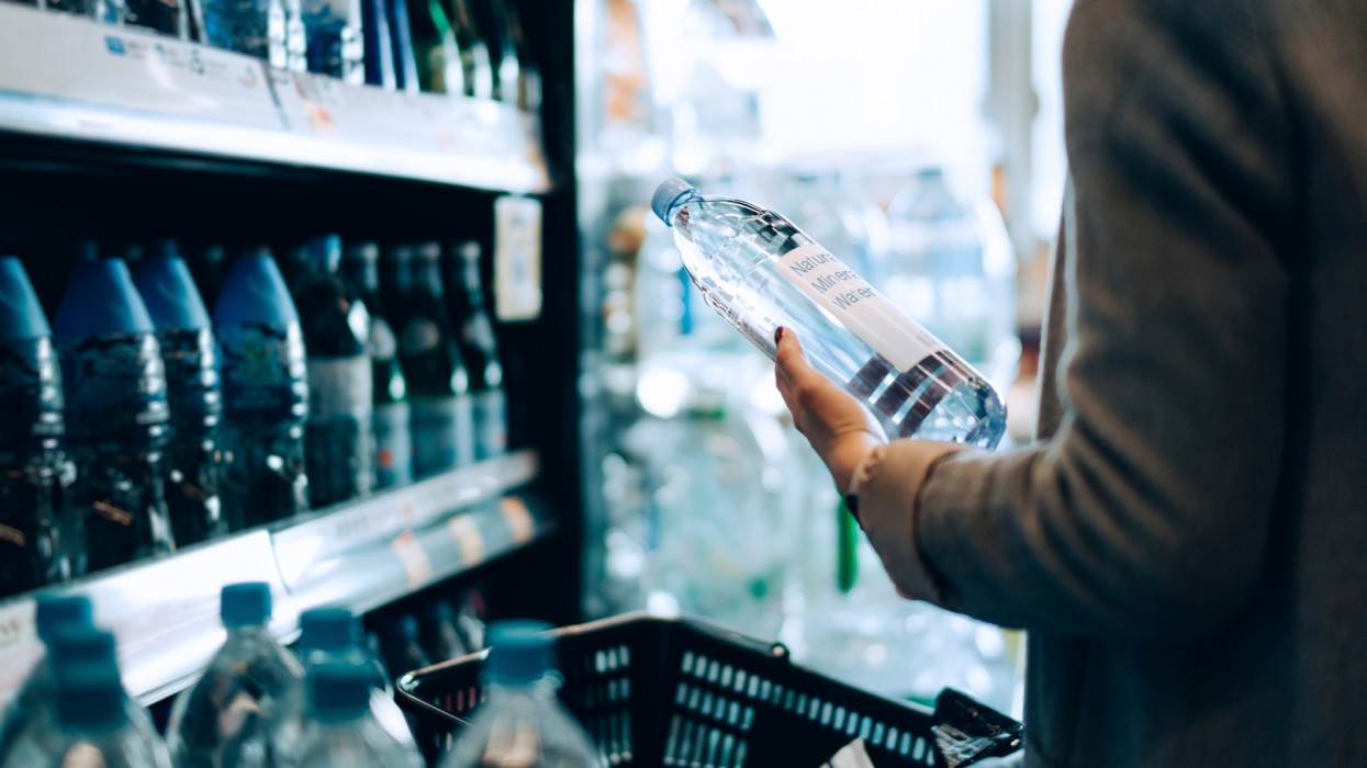 Close up of woman with shopping cart shopping for bottled water along the beverage aisle in a supermarket. Healthy eating lifestyle