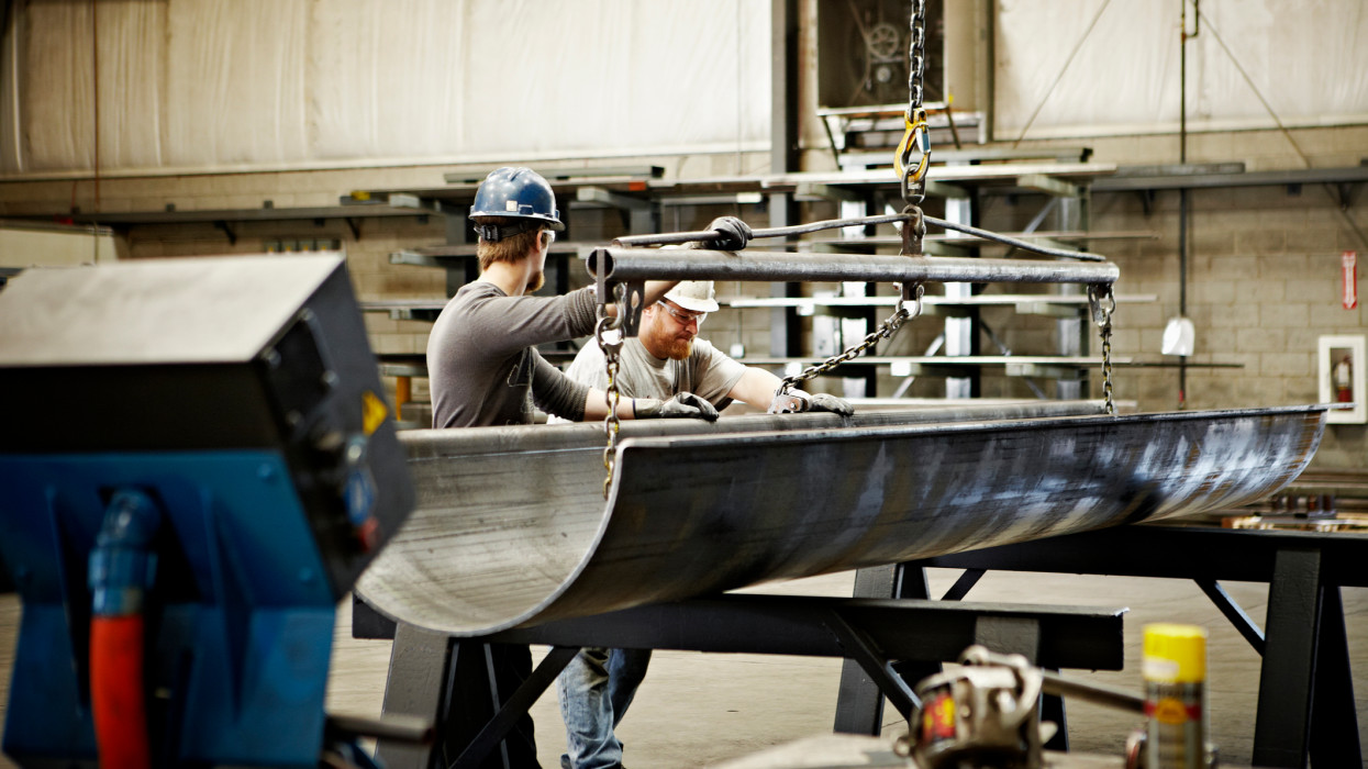 Steel workers adjusting position of brake press formed steel with crane