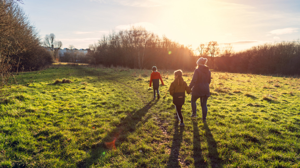 A mother and her two young sons walking in a country park in low winter sunlight, with their long shadows stretching towards the viewer.