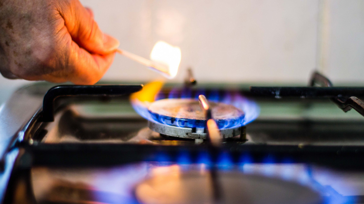 A match from the left corner lights the blue gas flame while one is already on in the foreground