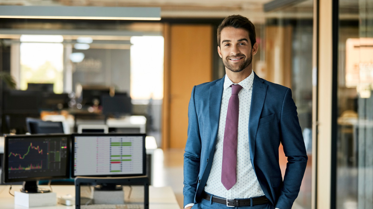 Portrait of smiling male entrepreneur standing with hands in pockets. Confident mid adult businessman is in creative office. He is wearing suit.