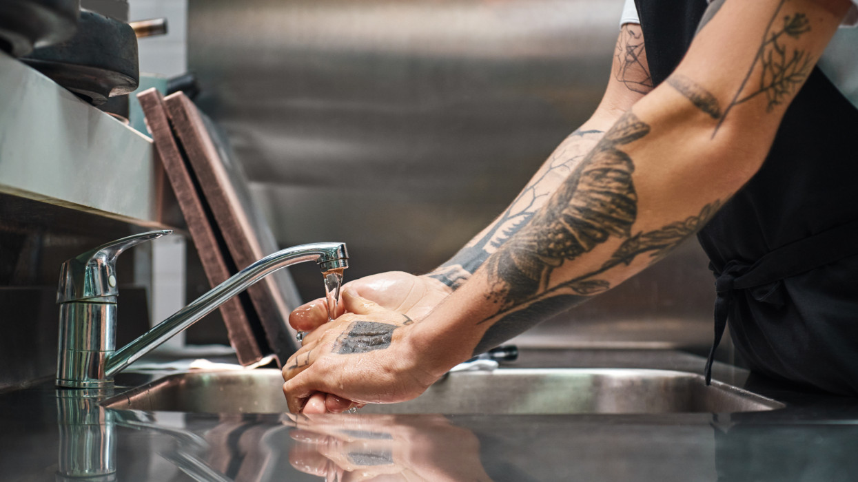 Before cooking...Close up photo of chef carefully washing his hands with different tattoos in a restaurant kitchen. Cropped view