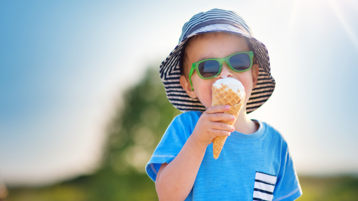 Happy child eating ice cream outdoors in summer. Portrait of a boy in sunglasses on sunny day