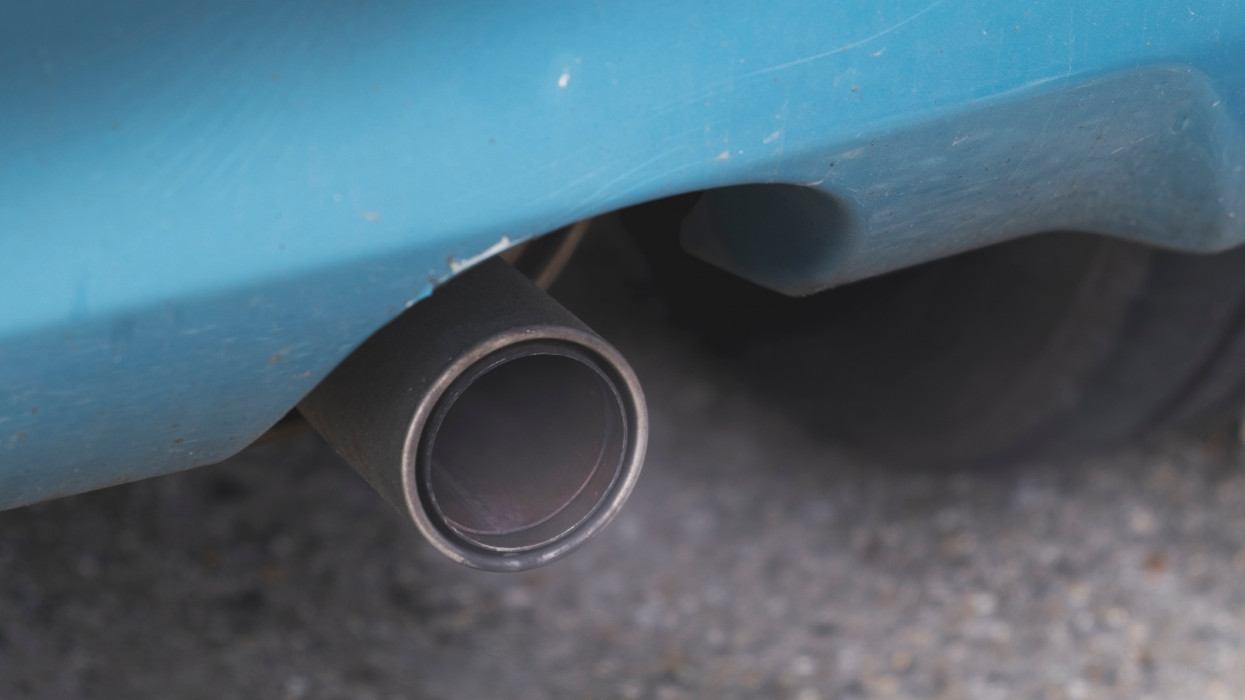 Close-up of a car exhaust emitting fumes, cyan blue car, worn frame