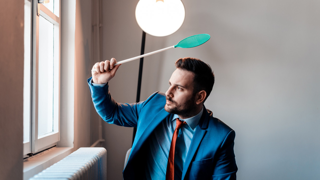 Attractive businessman with fly swatter. Annoyed men in a suit hitting a fly with fly swatter.