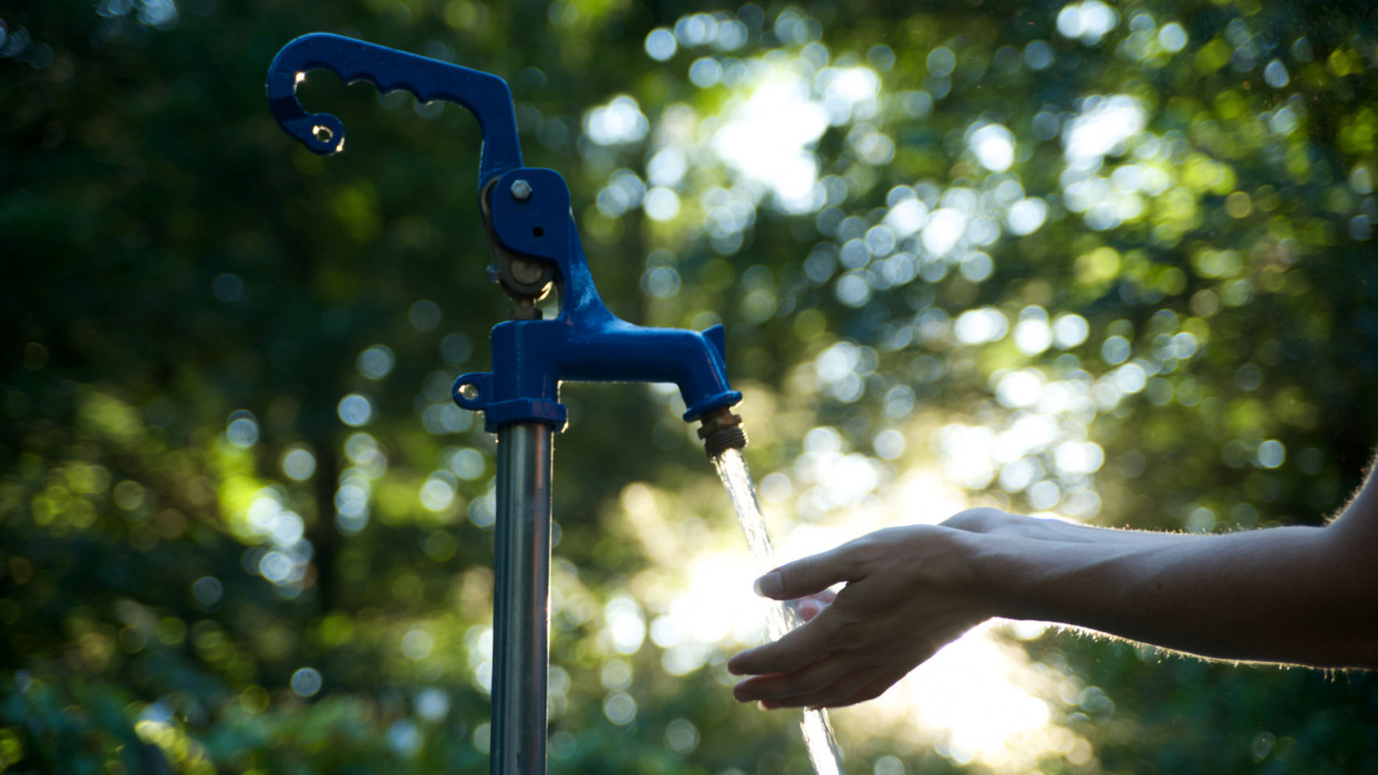 Woman washes hands under water spigot.