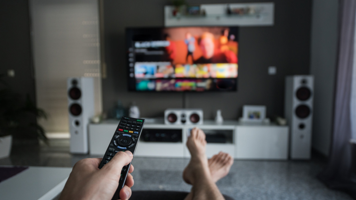 A young man is browsing through television channels with a remote control.