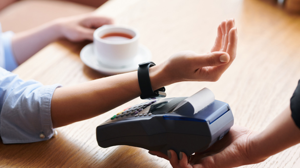 Close-up of unrecognizable woman putting wristwatch to payment terminal while making contactless payment in cafe smart watch pay