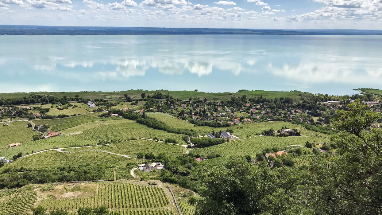 Top view of Lake Balaton with a village on the shore with a surface of water, which reflects the sky with clouds.