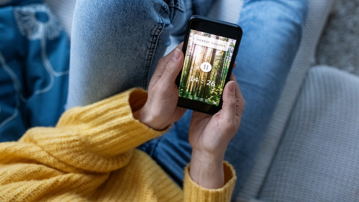 Closeup of a woman at home using mindfulness app to relax. Female listening to natures sounds on mobile app to meditate. Cell phone in hand of a woman.