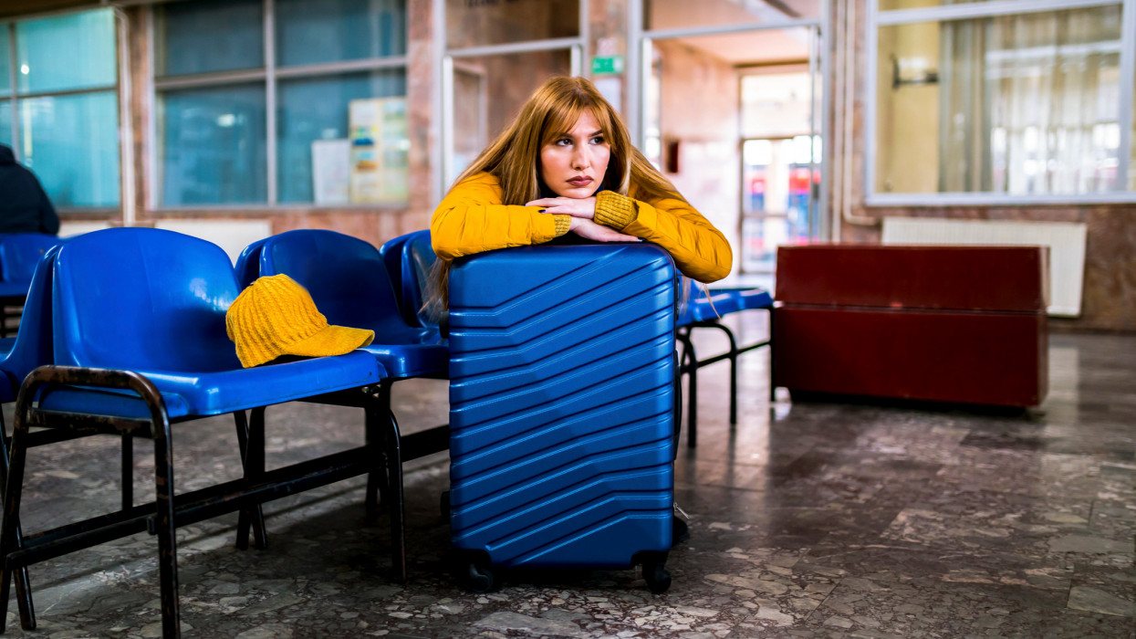 Young woman with suitcase sitting bored wait a time for traveler trip at train station