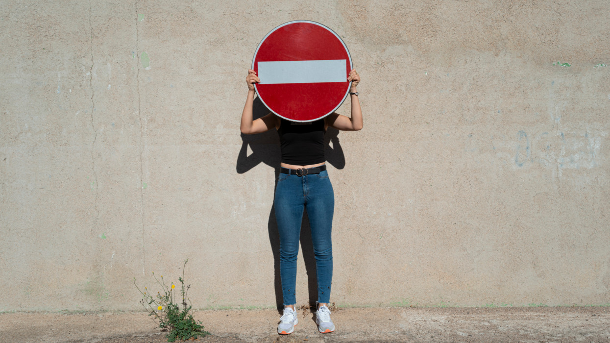 Young woman covering her face with a no entry sign