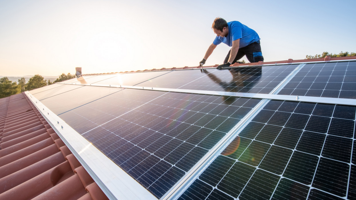 kneeling professional fixing solar panels from the top of a house roof, side view of the roof with sun reflection