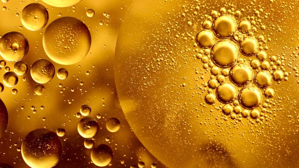 Full frame macro photography of gold-colored water and oil, forming an abstract pattern of circles and bubbles.