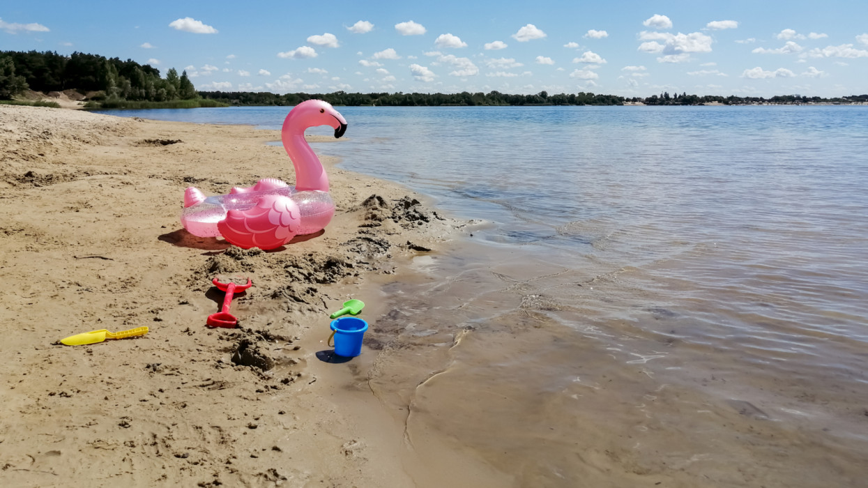 On the beach there are childrens toys and an inflatable circle in the form of flamingos. On the shore of the lake are decal toys for the baby and inflatable circle flamingos.