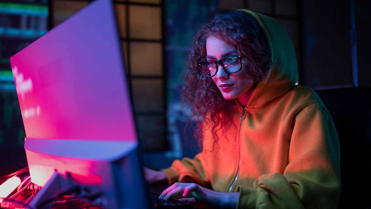 Young hacker woman working on computer alone in dark place.