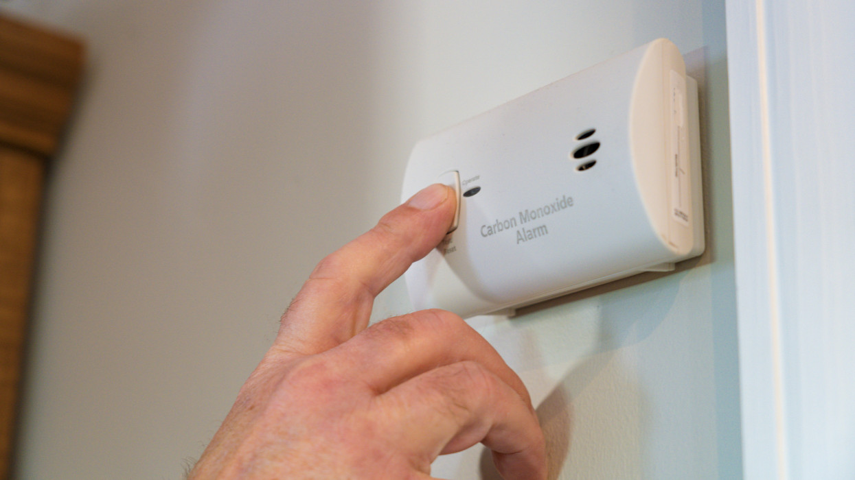 A hand punching a test button on an electrical Carbon Monoxide Alarm