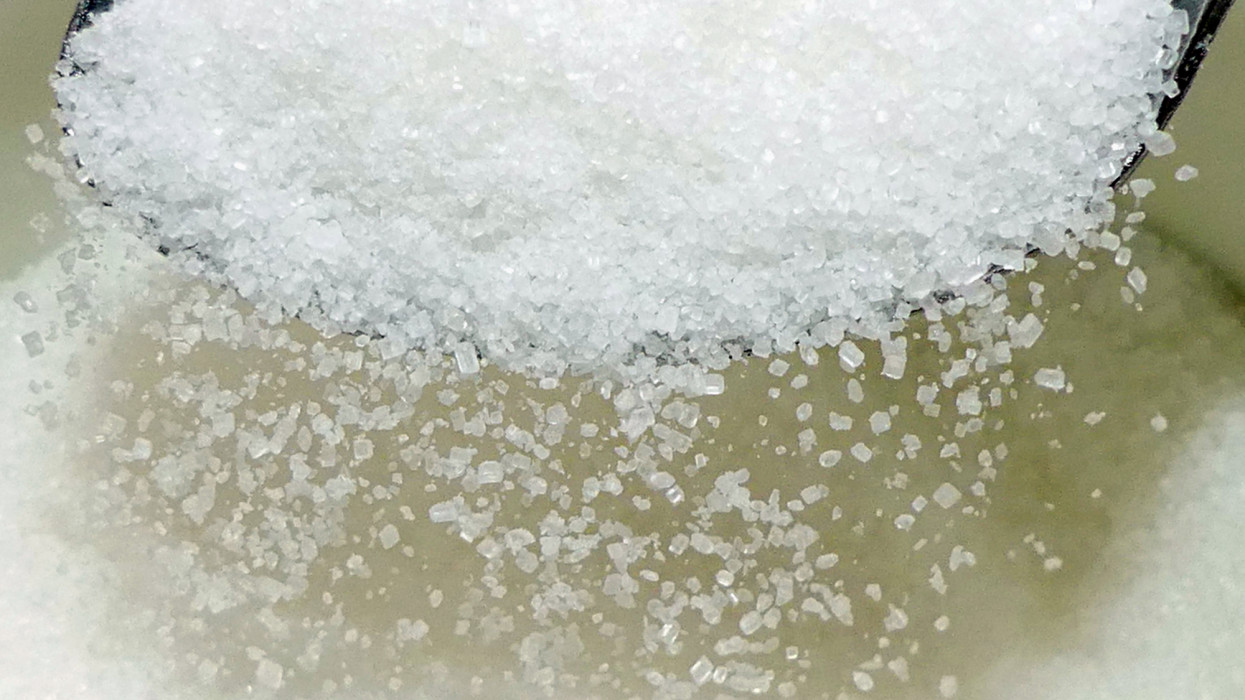 Refined white sugar, closeup falling from spoon. Health risksdiabetes and obesity.